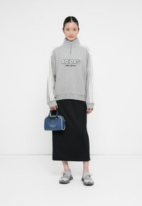 Sweatshirt cinza com fecho de correr e riscas brancas, saia maxi preta, sapatos cinzentos e uma mala azul com um logótipo. Texturas suaves por todo o lado.