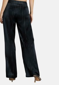 Zwarte satijnen wijde broek met zilveren verticale strepen. Glad textuur, hoge taille ontwerp, en gecombineerd met transparante haksandalen.