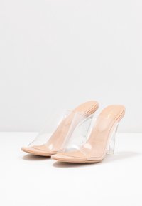 Klart klackade mules med en transparent ovandel och ljusbeige sula. Chunky, transparent blockklack ger stabilitet. Minimalistisk design.