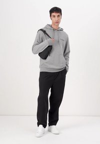 Felpa in pile grigia con tasca frontale, abbinata a pantaloni neri e sneakers bianche. Una piccola borsa a tracolla nera è indossata sulla spalla.
