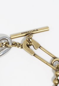 Złoty i srebrny metalowy zamek z projektem ogniw łańcucha. Posiada grawerunek "BIMBAY LOLA" na złotym pasku, łączy różnorodne faktury i wykończenia.