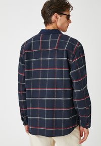 Camisa de franela a cuadros en navy con patrón de cuadrícula roja y blanca, puños abotonados y cuello clásico. Textura suave con un corte relajado.