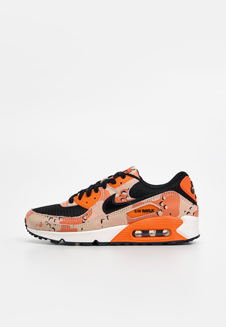 Las zapatillas Nike Air Max 90 cuentan con una parte superior de malla negra, acentos en naranja y beige, patrones únicos y una unidad de aire visible en la suela.