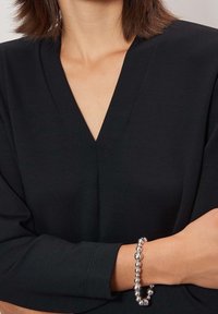 Černý top s výstřihem do V a tříčtvrtečními rukávy, doplněný stříbrným náramkem z korálků s hladkými a kulatými korálky.