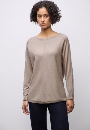 Haut beige à manches longues avec un col bateau, tissu doux, texture subtile et coupe légèrement ample, associé à un jean bleu.