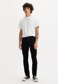 Melnas džinsa bikses un balts T-krekls ar apaļu kaklu. Bikses ir ar pieguļošu dizainu un gludu tekstūru. Sporta apavi ir klasiska auduma stila.