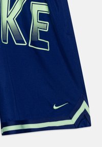 Pantalones cortos deportivos azul marino hechos de un tejido transpirable, con grandes letras en verde claro que dicen "NIKE" y un pequeño logo verde de Nike en el dobladillo.