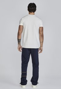 Camisa blanca de manga corta combinada con pantalones de chándal azul marino con una raya naranja. Material de algodón suave, corte relajado.
