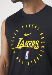 Camisola de basquetebol preta sem mangas com texto amarelo "LAKERS", logótipo circular e swoosh da Nike. Inclui logótipo da NBA abaixo. Tecido macio.