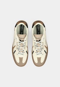 Balti un bēši sporta apavi ar brūniem un melniem akcentiem, ādas un tekstila materiāli, apaļa nospieduma purngala daļa, plakana zolīte un kontrastējošas auklas.