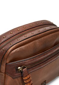 Sac à main en cuir marron avec des finitions cloutées, fermetures éclair doubles et un détail de bandoulière tressée. Surface texturée avec un léger éclat.