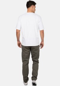 T-shirt blanc à manches courtes avec un col rond, associé à un pantalon vert olive. La tenue présente une coupe décontractée et un design simple.