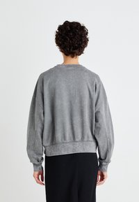 Sudadera gris con un lavado deslavado, cuello redondo y hombros caídos; cuenta con puños y dobladillo de canalé, corte relajado y una textura suave.