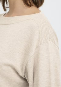Világos bézs pulóver, laza szabással, kerek nyakkivágással és finom bordázott mintával a vállakon és az ujjakon.