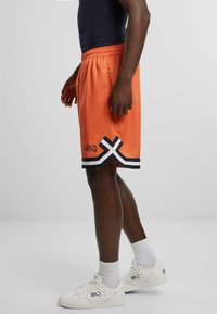 Orange mesh atletikshorts med sorte og hvide accenter samt et stiliseret logo. Shortsene har en afslappet pasform og elastisk talje.