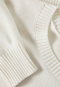 Kermaknsittupaito, jossa on ribbetty pyöreä kaula-aukko ja hihansuut, pehmeä rakenne ja hienovarainen kuvio kudonnassa.