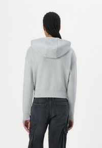 Felpa grigia rifinita, con cappuccio, orlo a costine e maniche lunghe. Indossata con pantaloni cargo scuri con molte tasche.