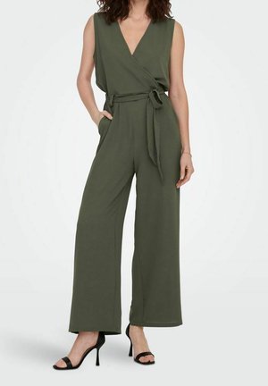 Combinaison sans manches vert olive à enfiler avec jambes larges, ceinture à nouer à la taille et sandales noires à talons hauts et bouts ouverts.