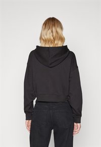 Haut cropped noir avec une capuche, coupe ample et poignets côtelés. Associé à un jean en denim noir taille haute, présentant une texture lisse.