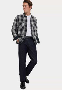Czarna i biała koszula w kratę z kołnierzykiem, zestawiona z ciemnymi spodniami i czarnymi butami, o luźnym kroju i detalach w postaci guzików.