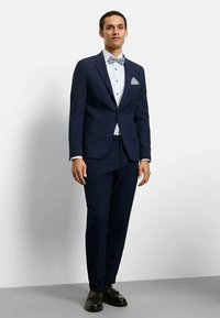 Navy suit with a fitted jacket, white shirt, dotted bow tie, and pocket square. Black shoes complete the formal attire.