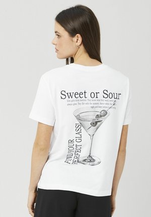 T-shirt blanc en coton avec un imprimé graphique d'un verre de martini et le texte « Sweet or Sour » au dos. Manches courtes, coupe décontractée.