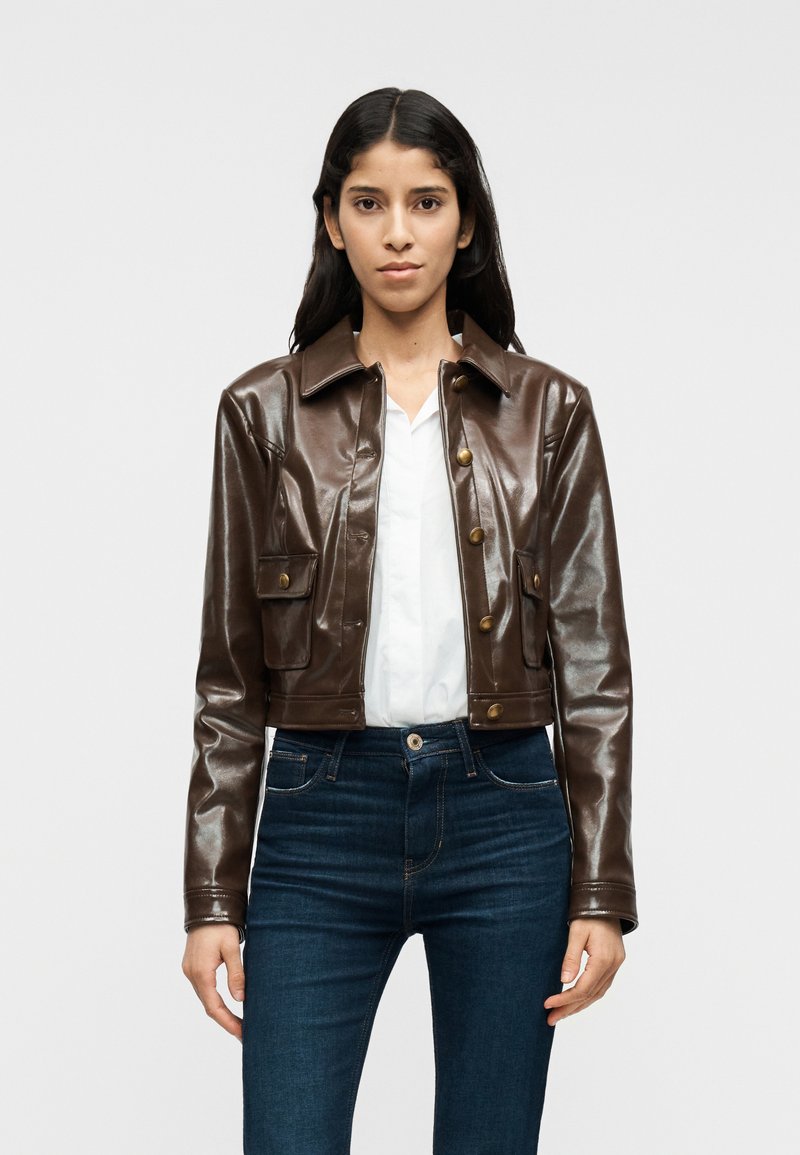 Καφέ μπουφάν cropped από ψεύτικο δέρμα με γιακά, κλείσιμο με κουμπιά στο μπροστινό μέρος, δύο τσέπες στο στήθος και γυαλιστερό φινίρισμα.