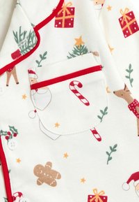 Pijamas de algodón blancos con patrones festivos de regalos, bastones de caramelo, renos y hombres de jengibre, con ribetes rojos y un bolsillo en el pecho.