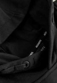 Črn AllSaints kapučin z vidno vrvico in več oznak blagovne znamke AllSaints v predelu ovratnika.