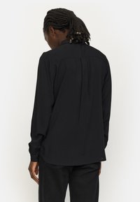 Čierna longsleeve košeľa s rovný strihom, záhybmi na chrbte, mäkkou látkou a detailmi gombíkových manžiet. Hladká textúra a minimalistický dizajn.