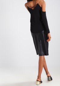 Svart ärmlös topp med korslagda band, i kombination med en svart läder midi-kjol och svarta sandaler med halkskydd som har metalliska detaljer.