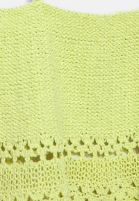 Tissu au crochet vert clair avec des motifs de points denses et ajourés disposés en bandes horizontales.