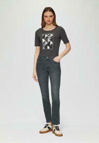 T-shirt gris avec un graphique géométrique, associé à un jean gris foncé et des baskets crème avec des lacets noirs et des semelles marron.