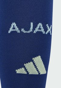 Tamno plave nogometne čarape s svijetloplavim izvezenim tekstom "AJAX" i trokutastim dizajnom logotipa, izrađene od teksturiranog pletiva.