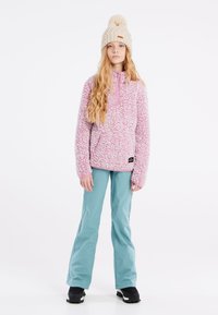 Pull en polaire rose avec un motif texturé, design à demi-fermeture éclair et poche avant ; associé à un pantalon bleu clair et des bottes d'hiver noires.