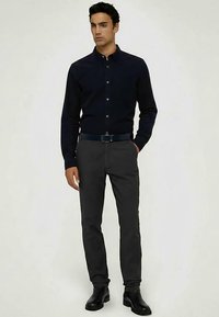 Tmavě námořnická košile na knoflíky z bavlny, doplněná o šedé kalhoty na míru. Oblečení má hladkou texturu a jednoduchý design.