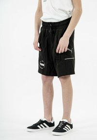 Pantalones cortos negros con cintura elástica, bolsillos laterales y detalle de logo. Combinados con zapatillas negras y blancas con tres rayas.