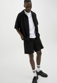 Black short-sleeve shirt with textured pattern, white T-shirt underneath, black shorts, white socks with black stripes, black shoes.