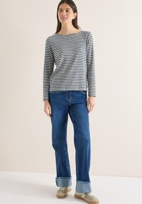 Chemise à manches longues rayée bleu marine et blanc, associée à un jean droit bleu avec ourlets retroussés, et des baskets beiges.