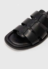 Black synthetic slide sandal featuring four wide straps, a padded insole, and a textured finish. Rounded toe and flat sole design.