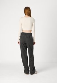 Top corto de manga larga color crema claro combinado con pantalones de pierna ancha en gris oscuro con cintura elástica. Tejido liso sin patrones visibles.