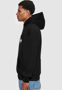 Czarna bluza z kapturem z przednią kieszenią. Wykonana z miękkiego, grubego materiału, z logo nadrukowanym na klatce piersiowej i ściągaczami przy mankietach.