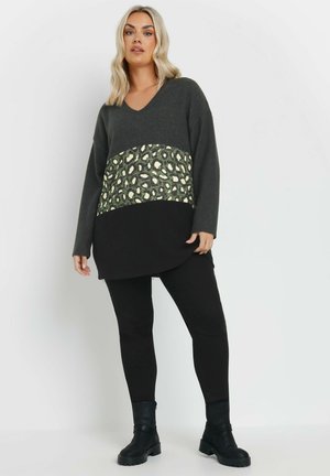 Maglione grigio a scollo a v con una fascia in stampa leopardata nei toni del verde e crema, abbinato a leggings neri e stivali alla caviglia neri. Vestibilità rilassata.
