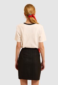 Crème top met korte mouwen en zwarte biezen, gecombineerd met een zwarte gestreepte rok. Haar vastgebonden met een rode sjaal, zichtbaar met een gladde, gestructureerde afwerking.