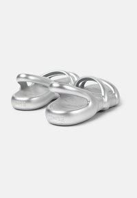 Silverfärgade sandaler med en slät, metallisk yta. Har två böjda remmar och en rund sula. Graverat varumärke på hälen.