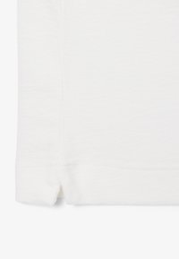 Nahaufnahme eines weißen Stoffsaums mit kleinem Seitenschlitz und sichtbaren horizontalen sowie vertikalen Nahtlinien.