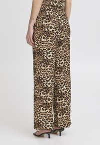 Bežové a hnedé nohavice so širokými nohavicami s leopardím vzorom, so elastickým pásom a hladkým povrchom. Zobrazené zozadu.