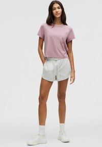 Top corto de manga corta en lavanda, combinado con pantalones cortos grises de cordón. Zapatillas blancas y calcetines hasta el tobillo completan el conjunto. Diseño sencillo.