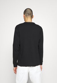 Černé tričko s dlouhým rukávem a kulatým výstřihem, vyrobené z bavlny. Má pohodlný střih a žebrované manžety, doplněné bílými kalhotami.