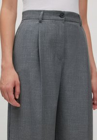 Graue, gepresste Hose aus strukturiertem Stoff mit Knopfverschluss und Seitentaschen, von der Taille bis zur Mitte des Oberschenkels abgebildet.